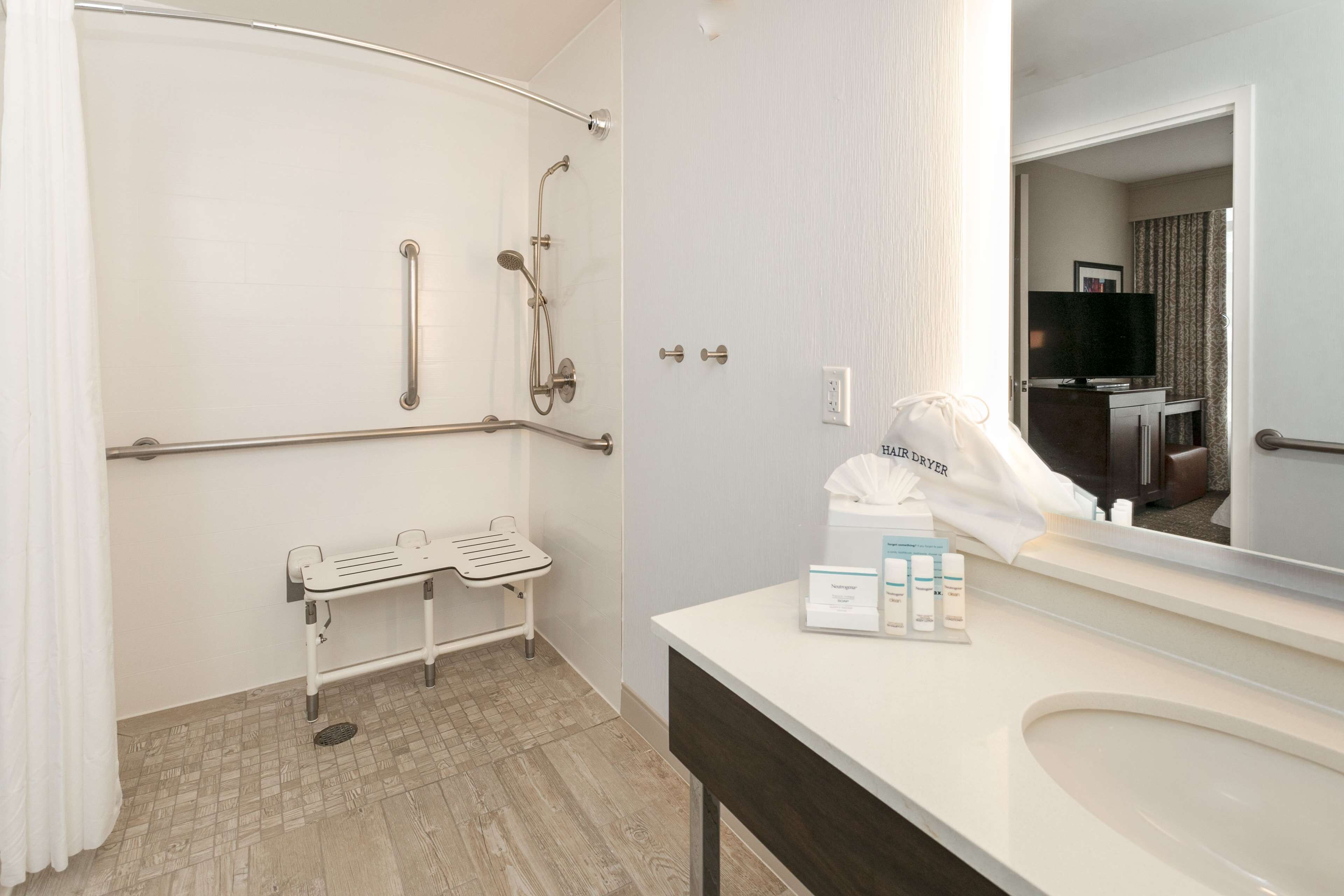 A bathroom with a shower, grab bars, a towel rack, and a vanity with a mirror.