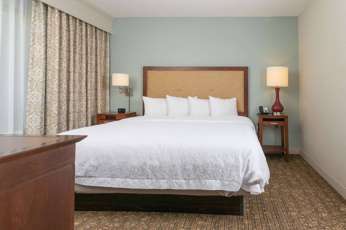 Een hotelkamer met een groot bed, twee nachtkastjes, een bureau en een raam met gordijnen.