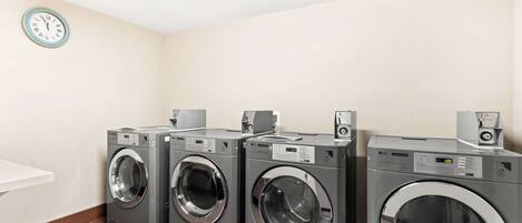 A laundry room with three front-loading washing machines, a clock on the wall, and a white sink.