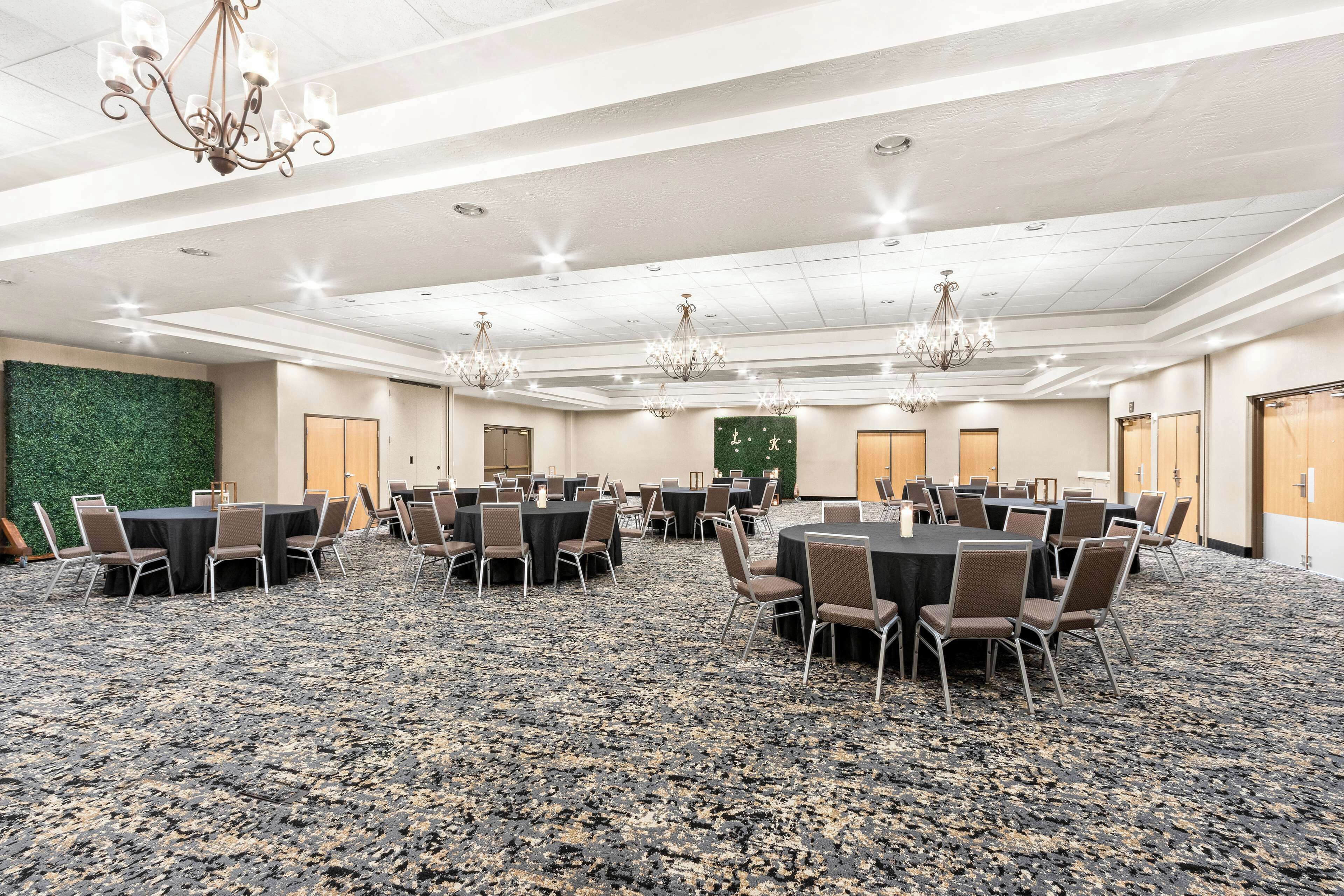 A conference room with multiple tables and chairs, carpeted flooring, chandeliers, and a green wall.