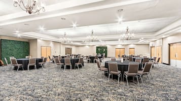 A conference room with multiple tables and chairs, carpeted flooring, chandeliers, and a green wall.