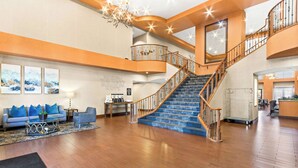A spacious lobby with a grand staircase, a seating area with blue cushions, and artwork on the walls. - Hampton Inn & Suites Phoenix-Goodyear (Goodyear)