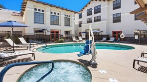 A pool area with lounge chairs, a hot tub, and a building with multiple windows and doors. - Hampton Inn & Suites Phoenix-Goodyear (Goodyear)