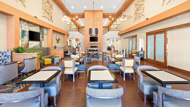 A spacious dining area with multiple tables and chairs, a central seating area, and a kitchen in the background. - Hampton Inn & Suites Phoenix-Goodyear (Goodyear)