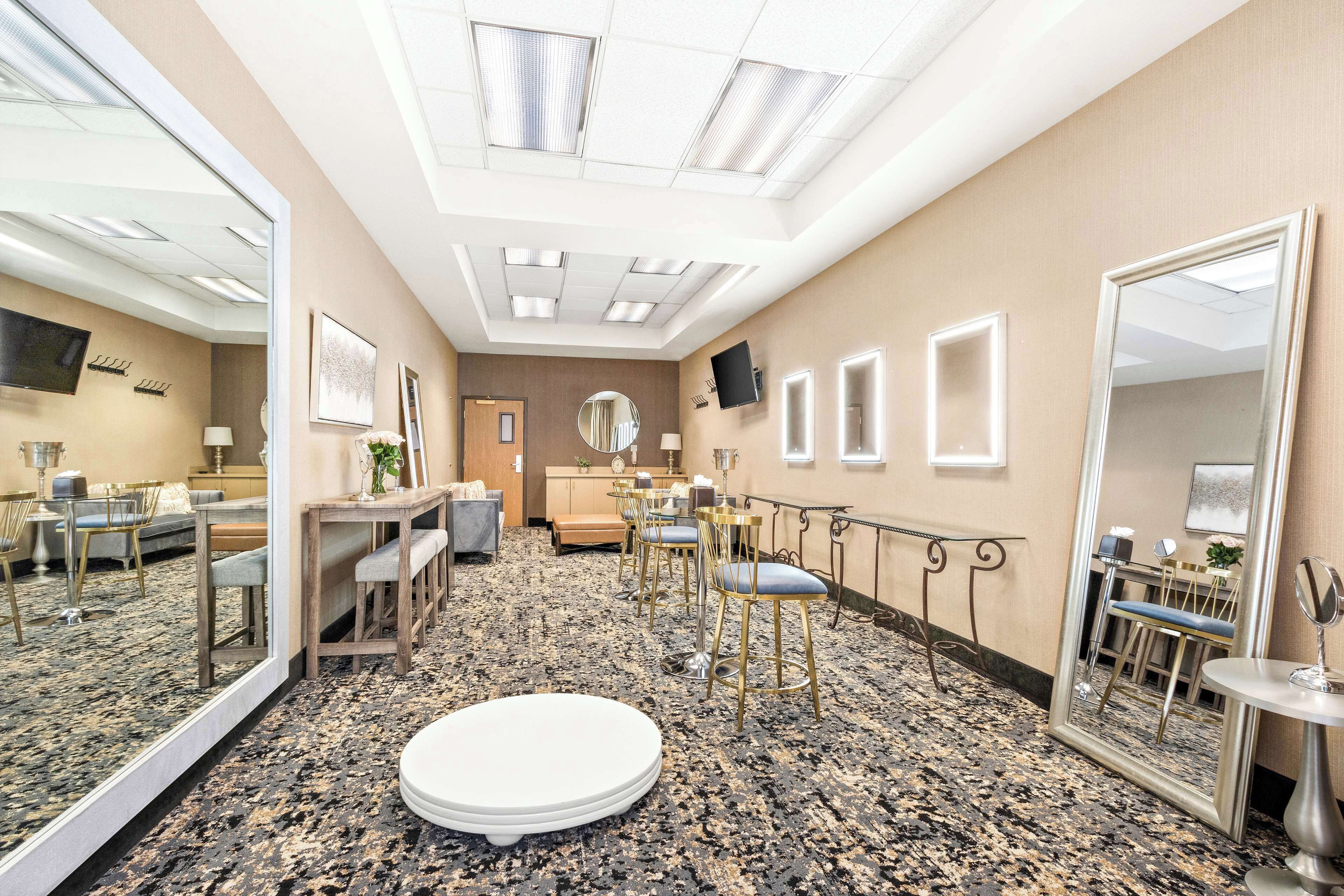 Una camera d'albergo con un grande specchio, un tavolo rotondo bianco e una zona salotto con poltrone e divano.