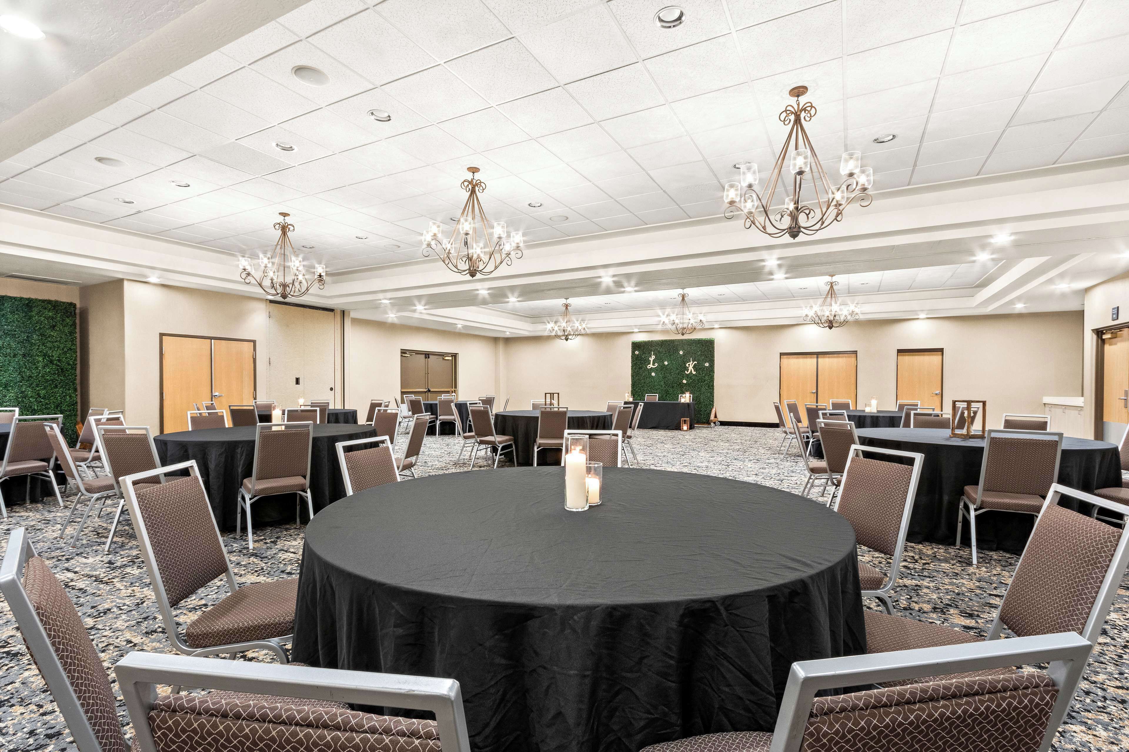 A conference room with round tables, chairs, chandeliers, and a green wall.