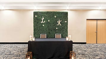Una sala de conferencias con una mesa negra, dos sillas, una pared verde decorada con las letras 'L' y 'K', y puertas de madera.