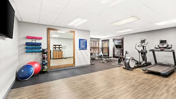 A modern gym with exercise equipment, a large mirror, and a television on the wall.