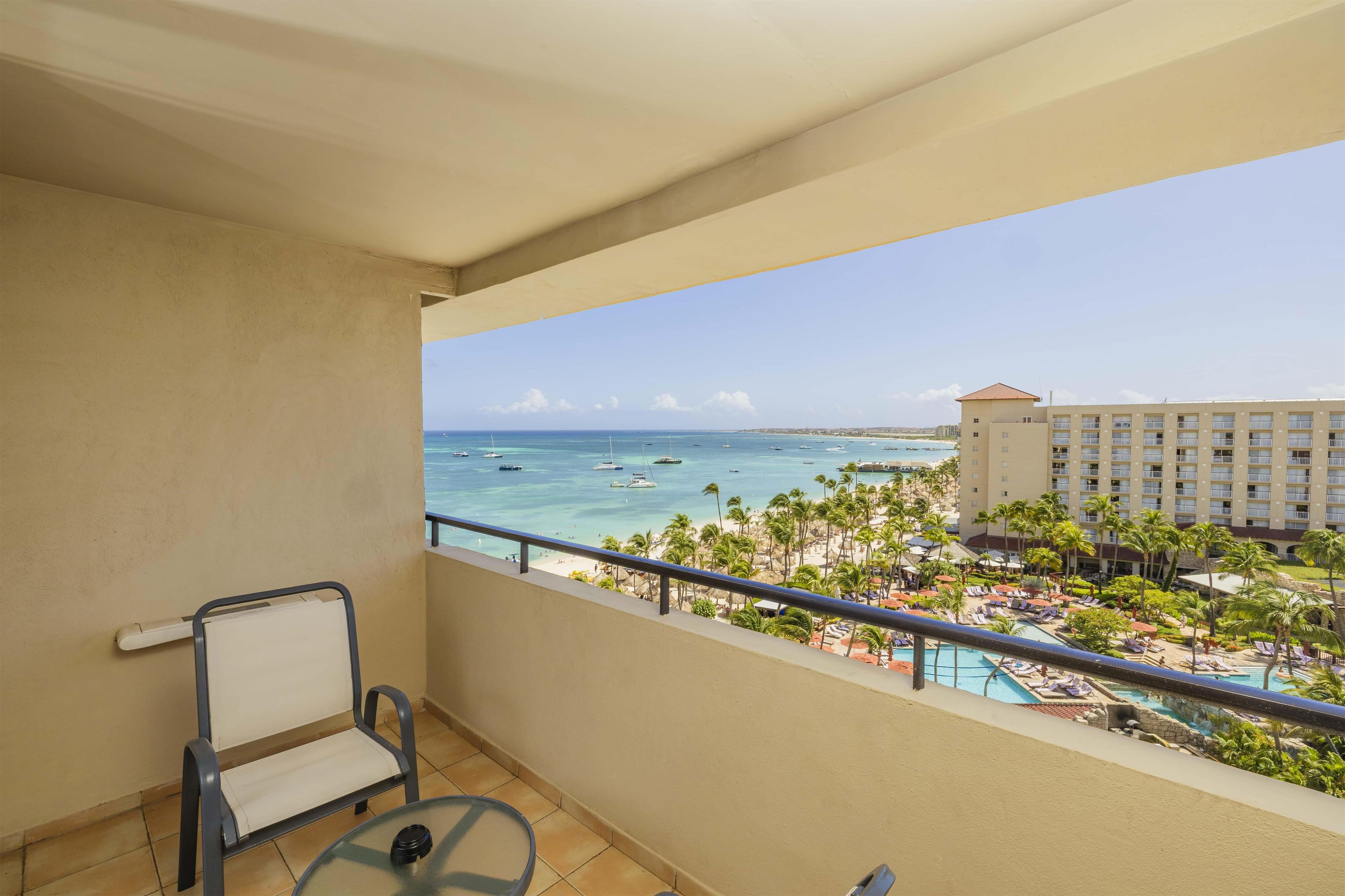 A balcony with a view of a beach, a pool area, and a hotel building.