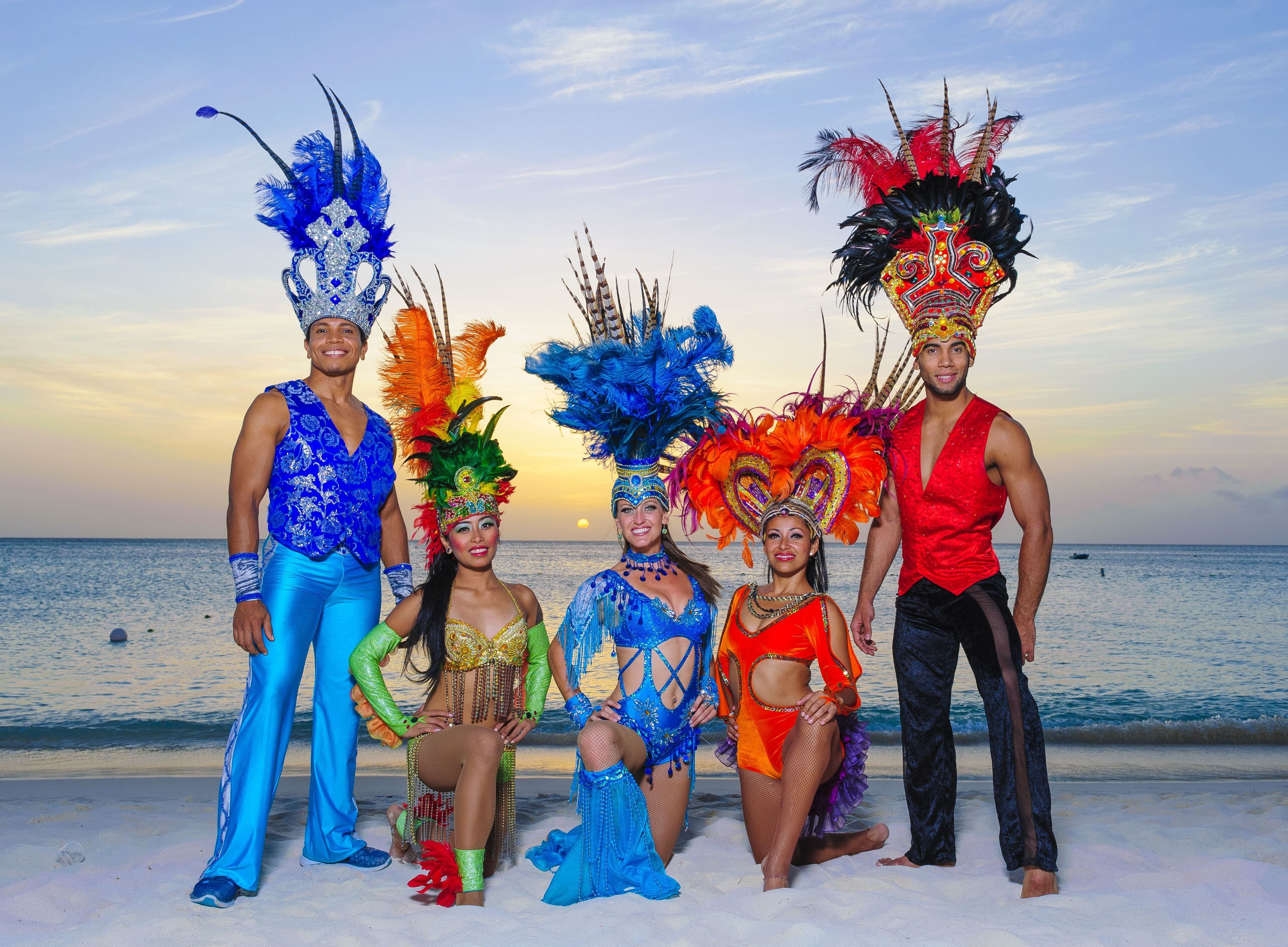 A group of people in colorful costumes on a beach with the ocean in the background.