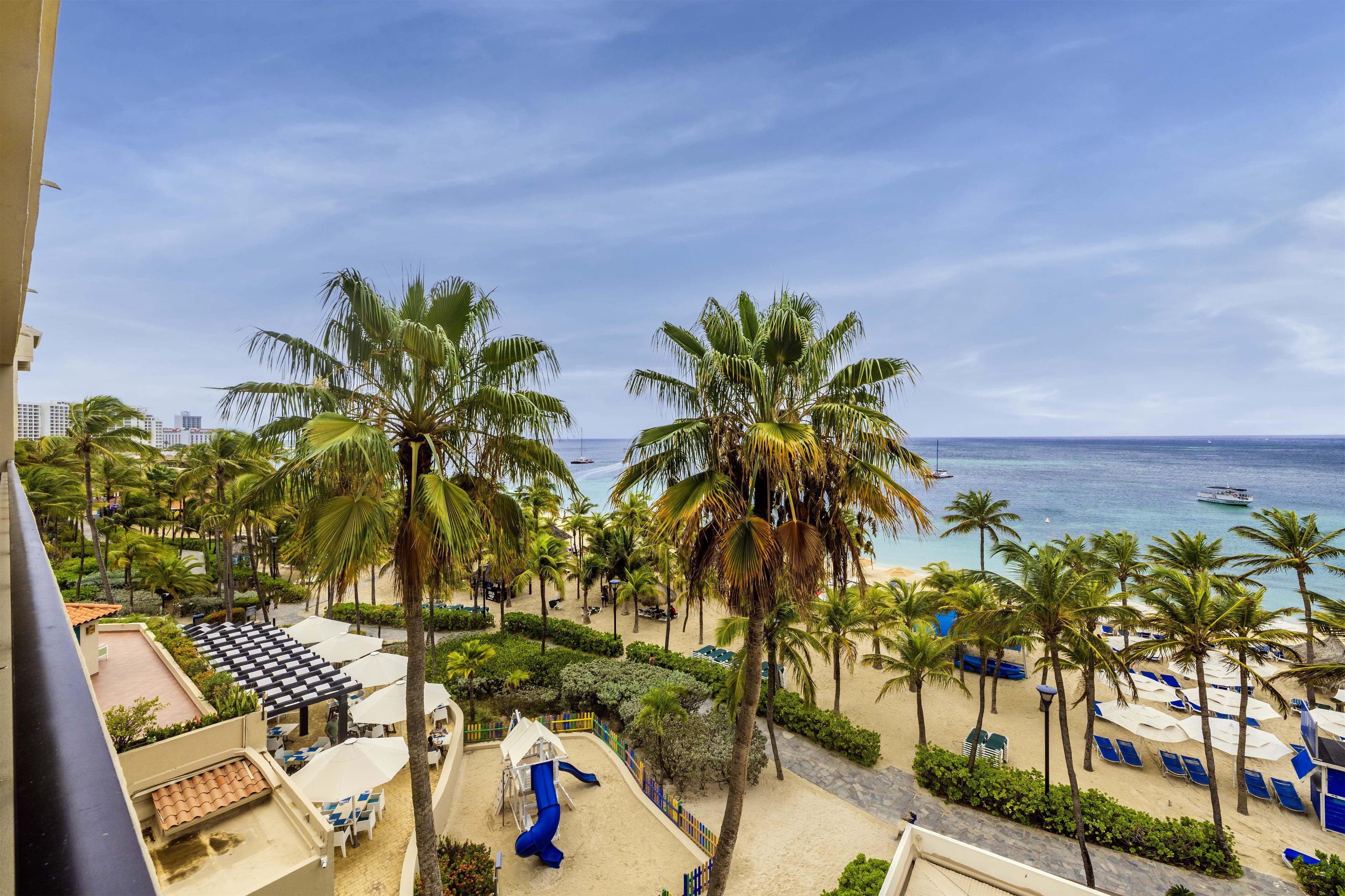 A beach view with palm trees, a playground, and a clear sky.