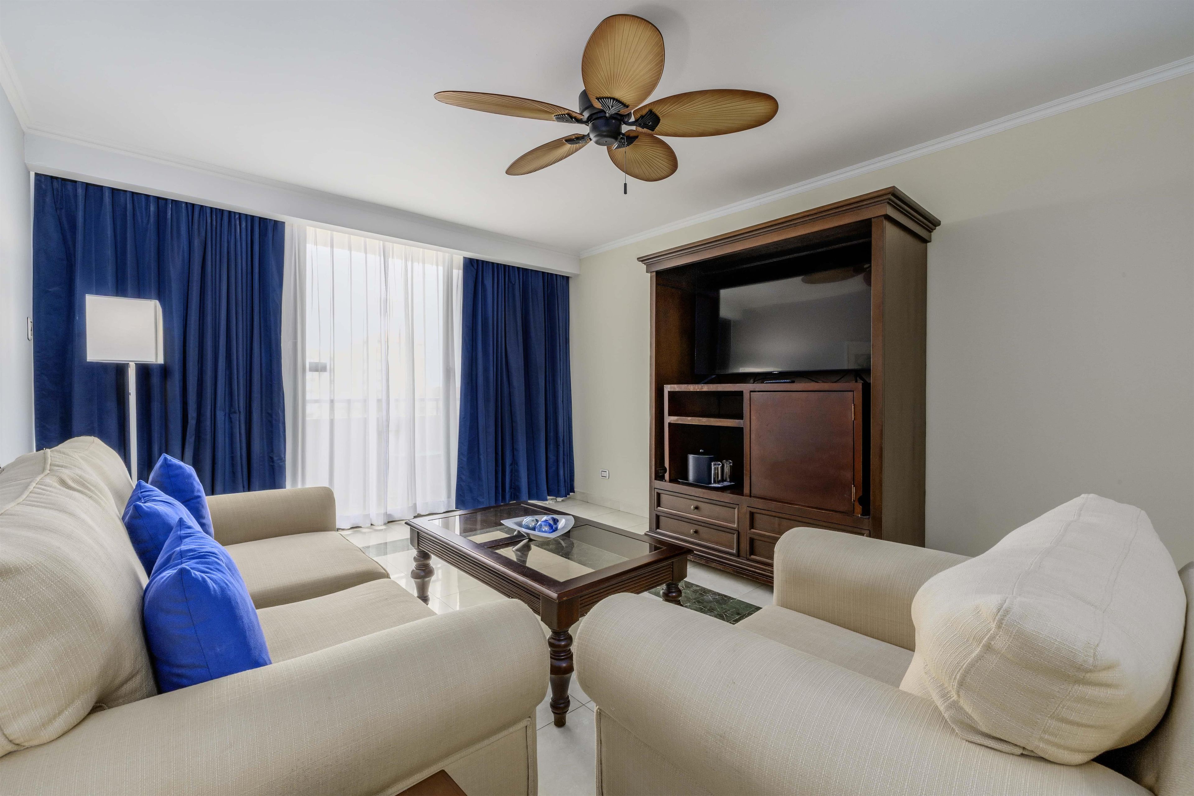 Uma sala de estar com ventilador de teto, mesa de centro de vidro e televisão.