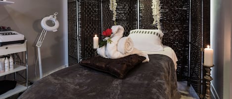 A neatly arranged bedroom with a bed, a bedside table, a lamp, and a decorative partition with hanging flowers.