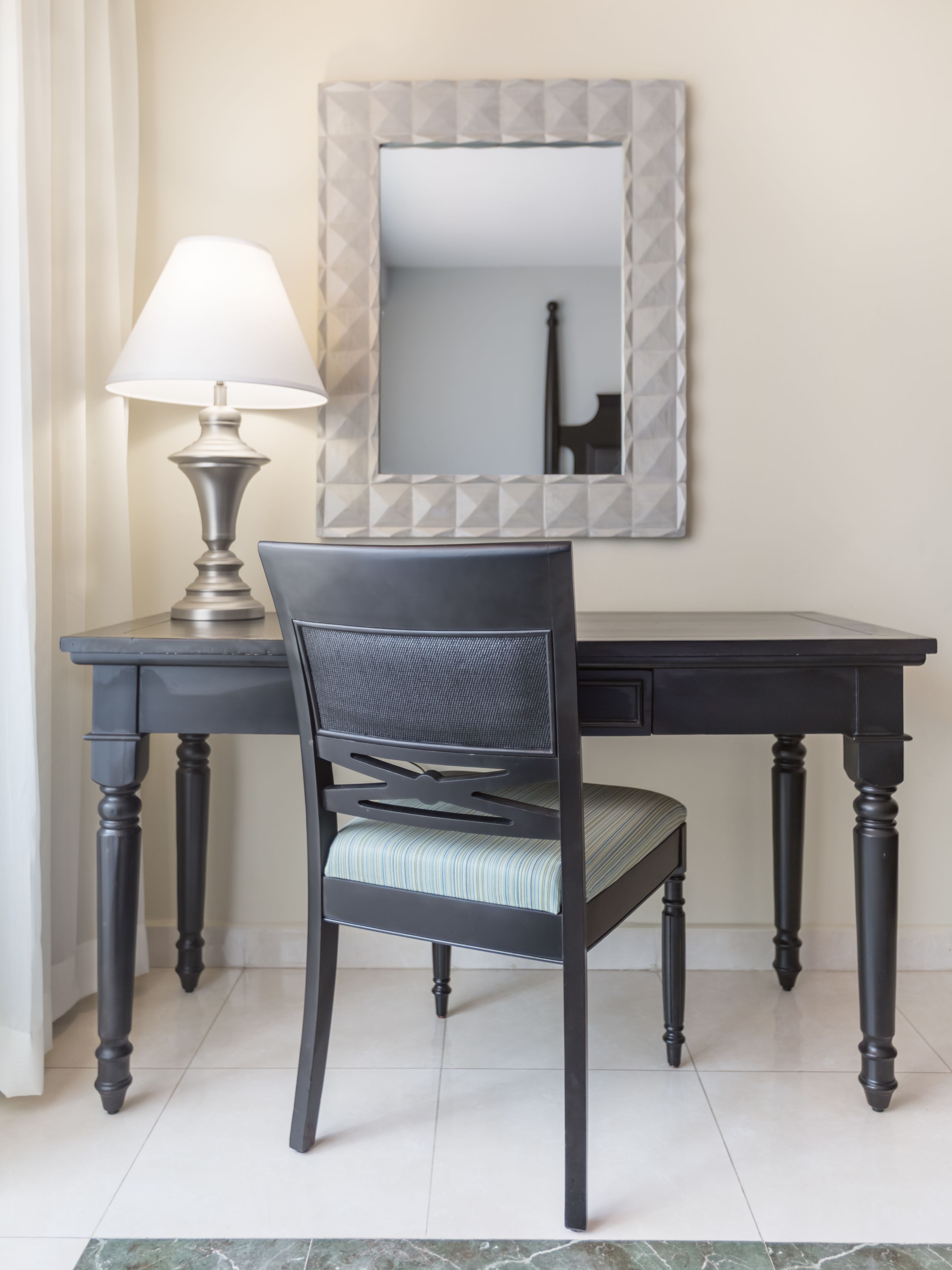 A dark wooden desk with a chair, a lamp, and a mirror.