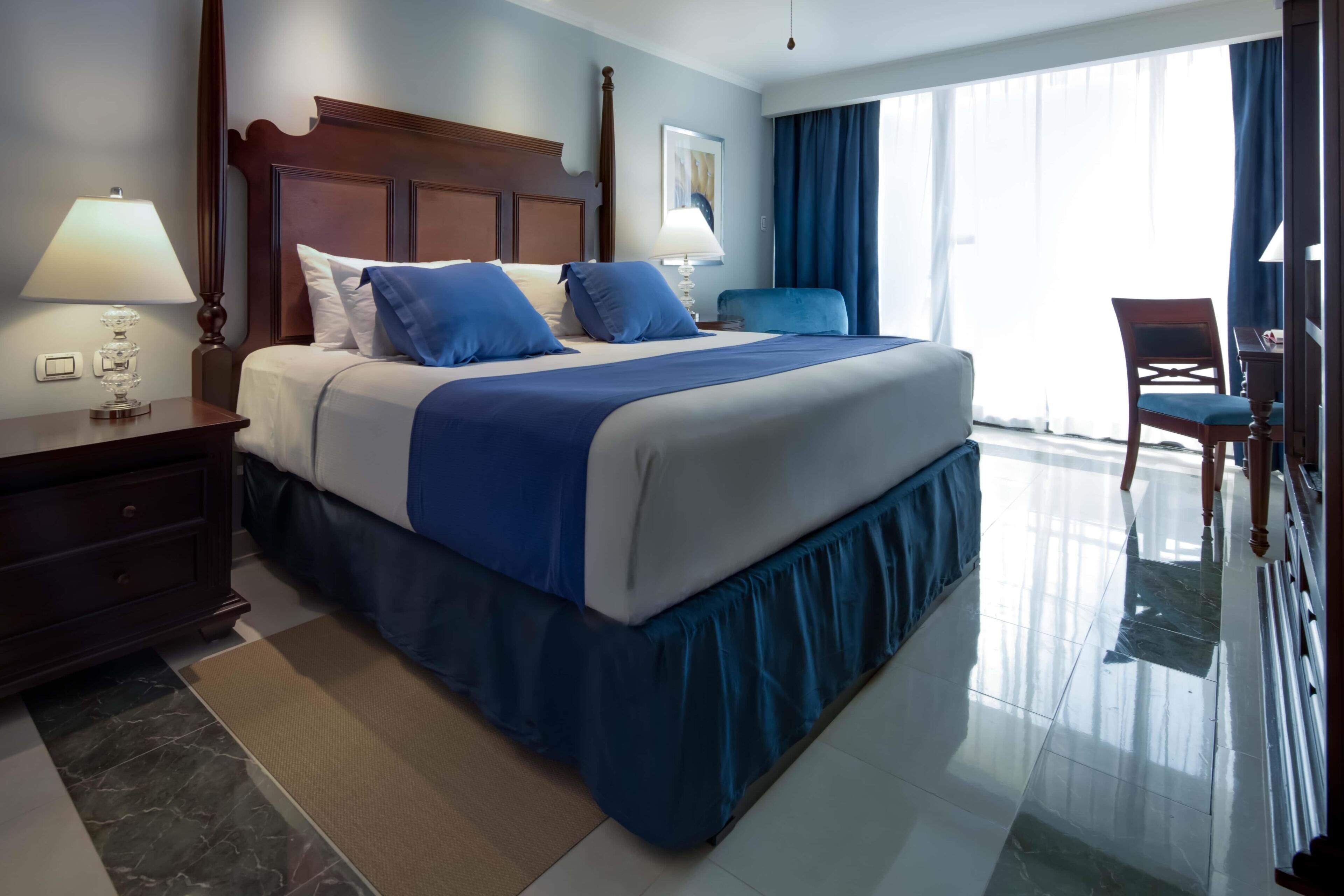 Habitación de hotel con una cama grande, una mesita de noche, un escritorio, una silla y vistas al exterior.