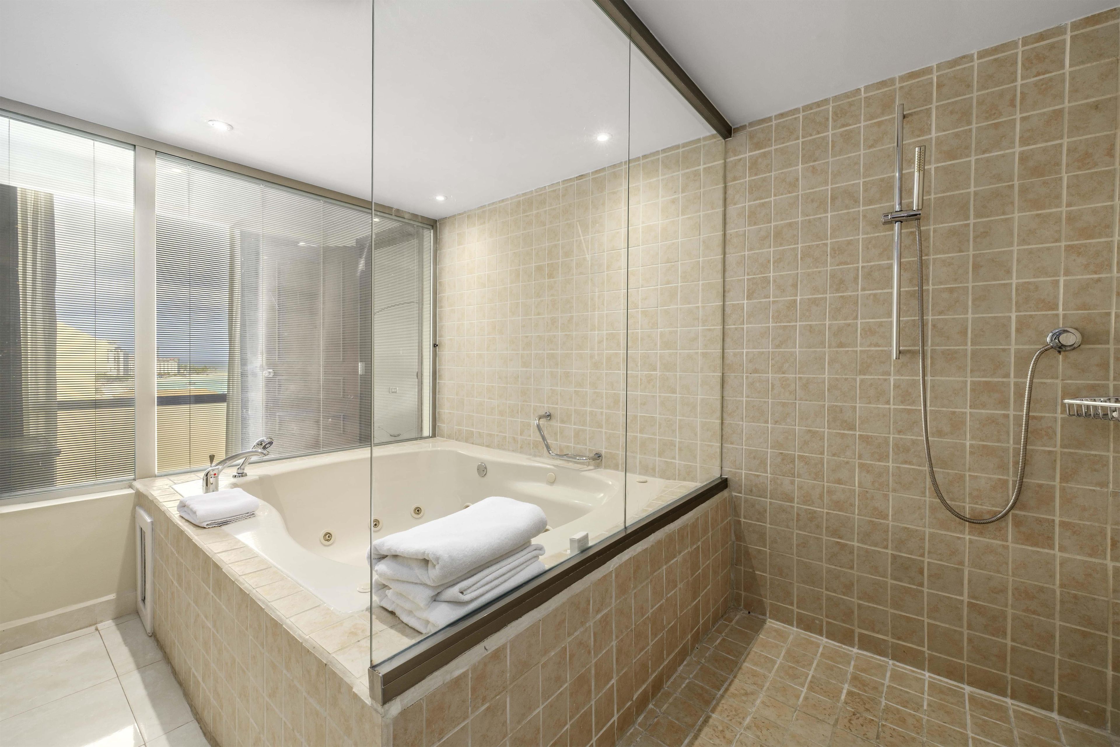 A modern bathroom with a glass-enclosed bathtub, a shower area, and a large window with blinds.