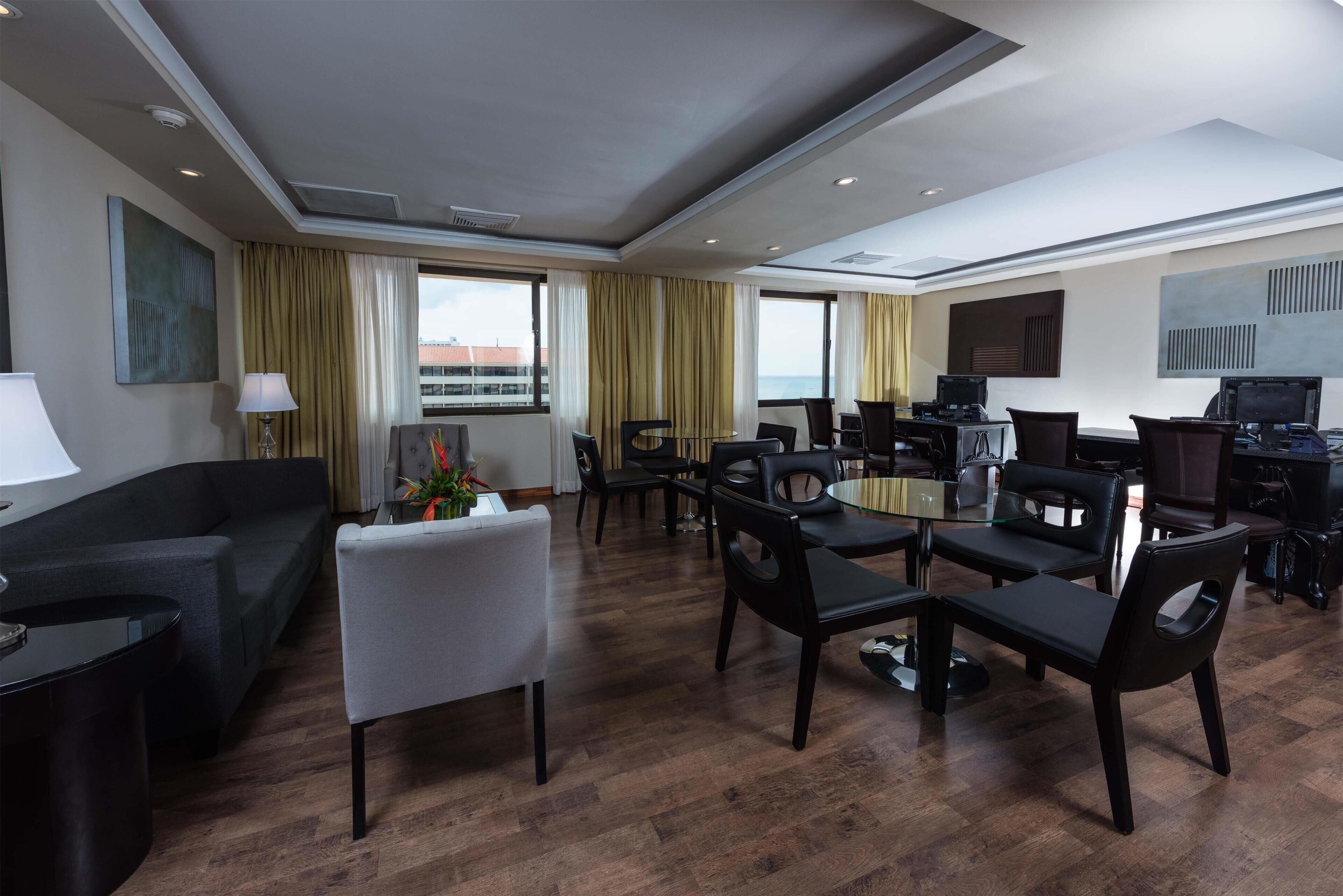 Ein Hotelzimmer mit Essbereich, Sofa, Fernseher und Blick auf die Stadt.