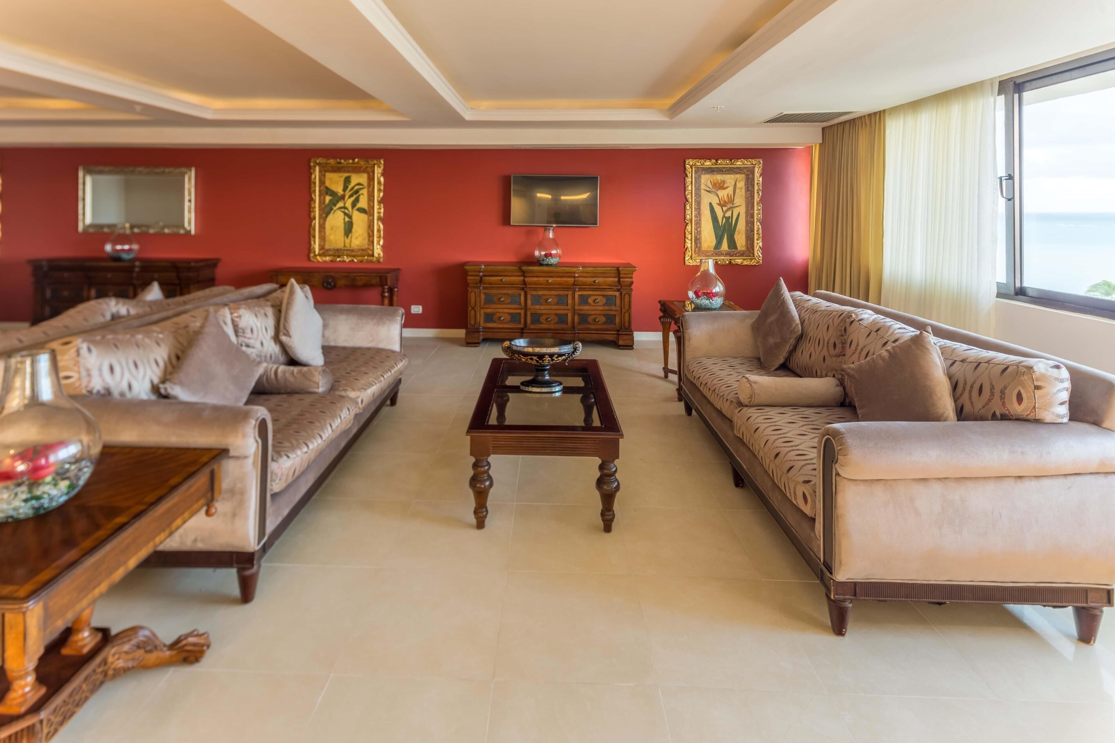 A spacious living room with a sofa set, a coffee table, a television, and a large window with curtains.