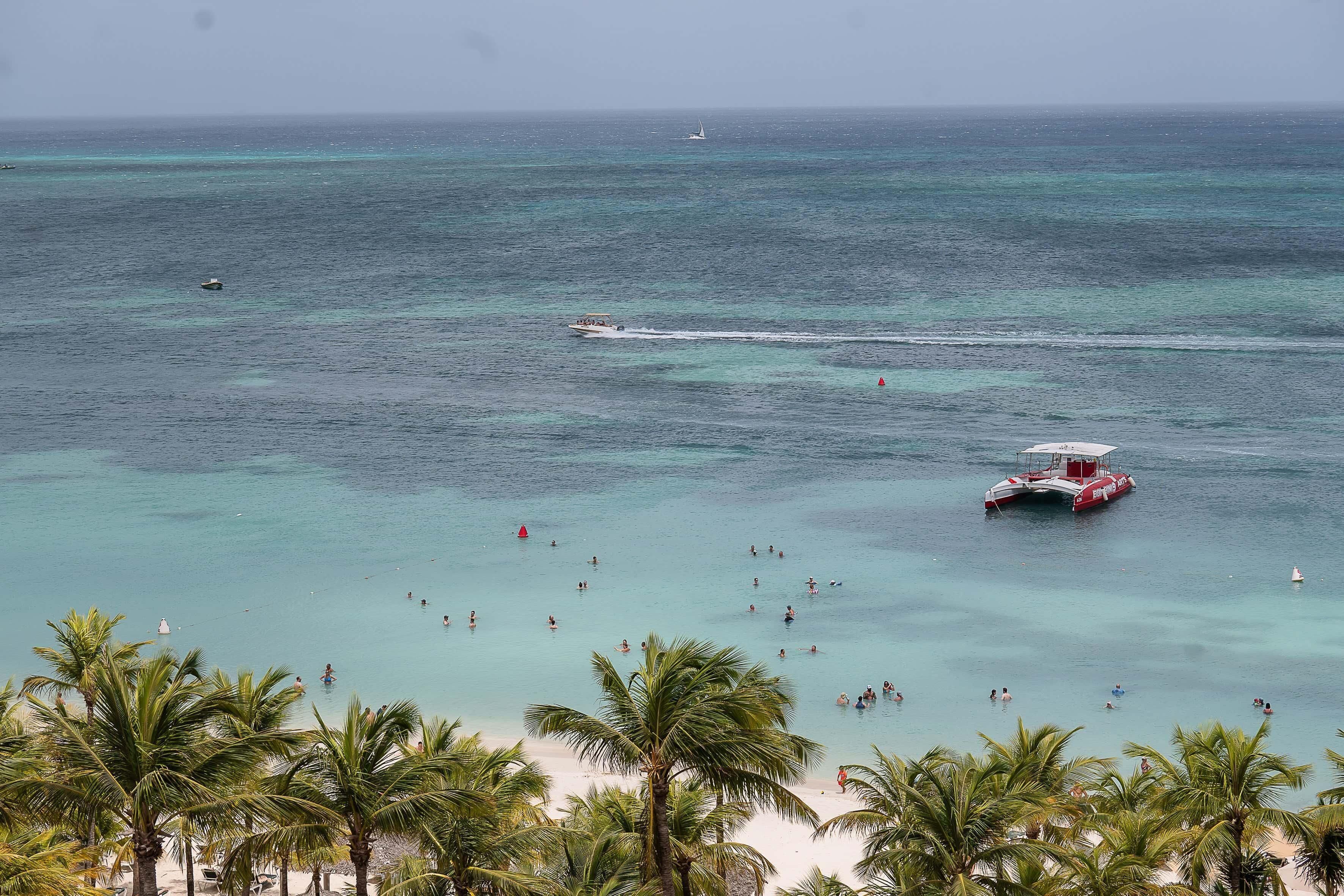 A beach with clear turquoise water, a boat, and palm trees.