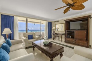 A hotel room with a balcony, a television, a dining table, and a sofa.