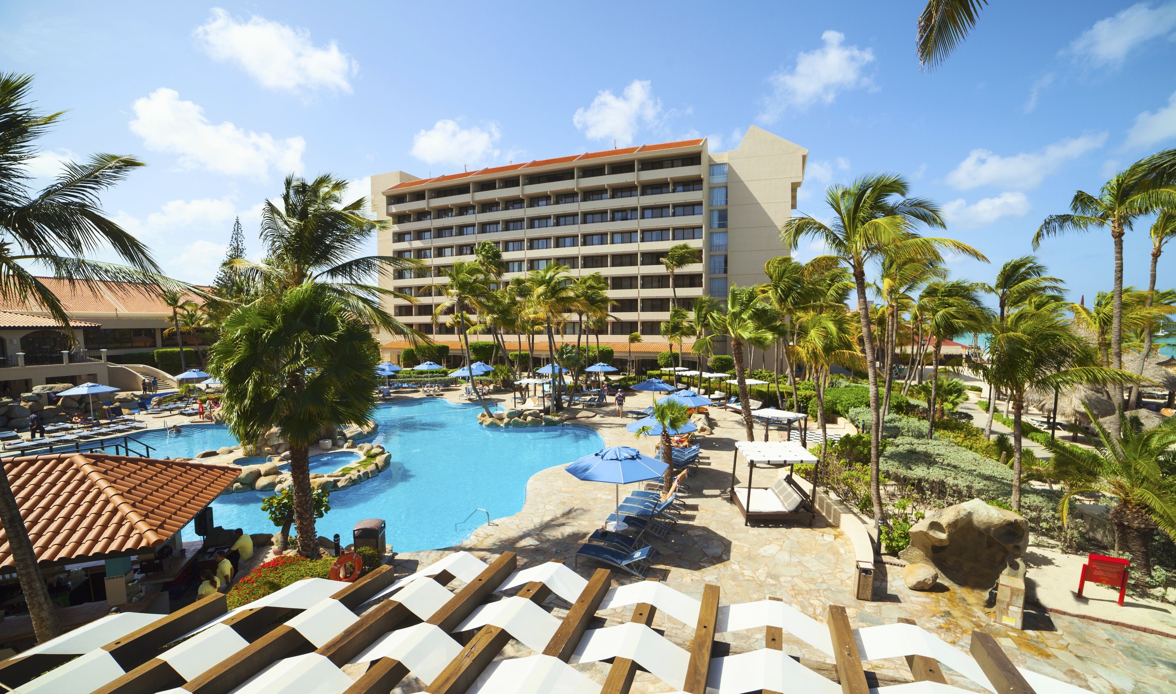 A resort with a large pool, palm trees, and a multi-story building.