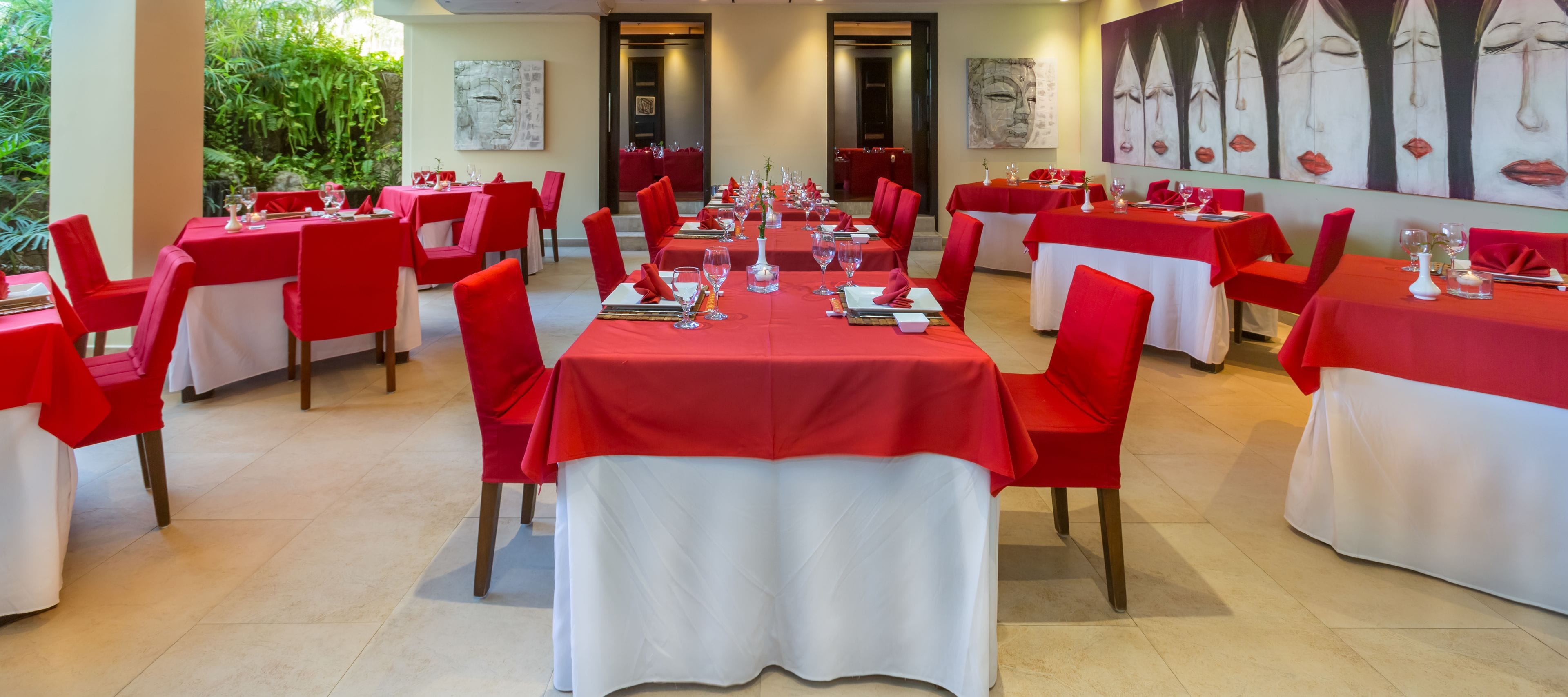 Ein Restaurant mit roten und weißen Tischdecken, roten Stühlen und Blick auf Grünflächen.