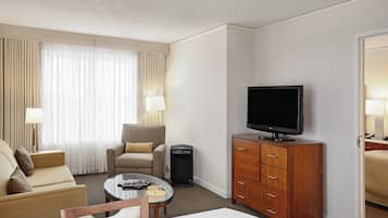 A hotel room with a sofa, armchair, TV, and a small table with a lamp.