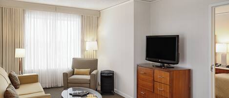 A hotel room with a sofa, armchair, TV, and a small table with a lamp.