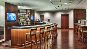 A bar area with a counter, stools, and a television screen. There are shelves with bottles and a sign indicating an exit. - InterContinental Suites Hotel Cleveland by IHG (Cleveland)