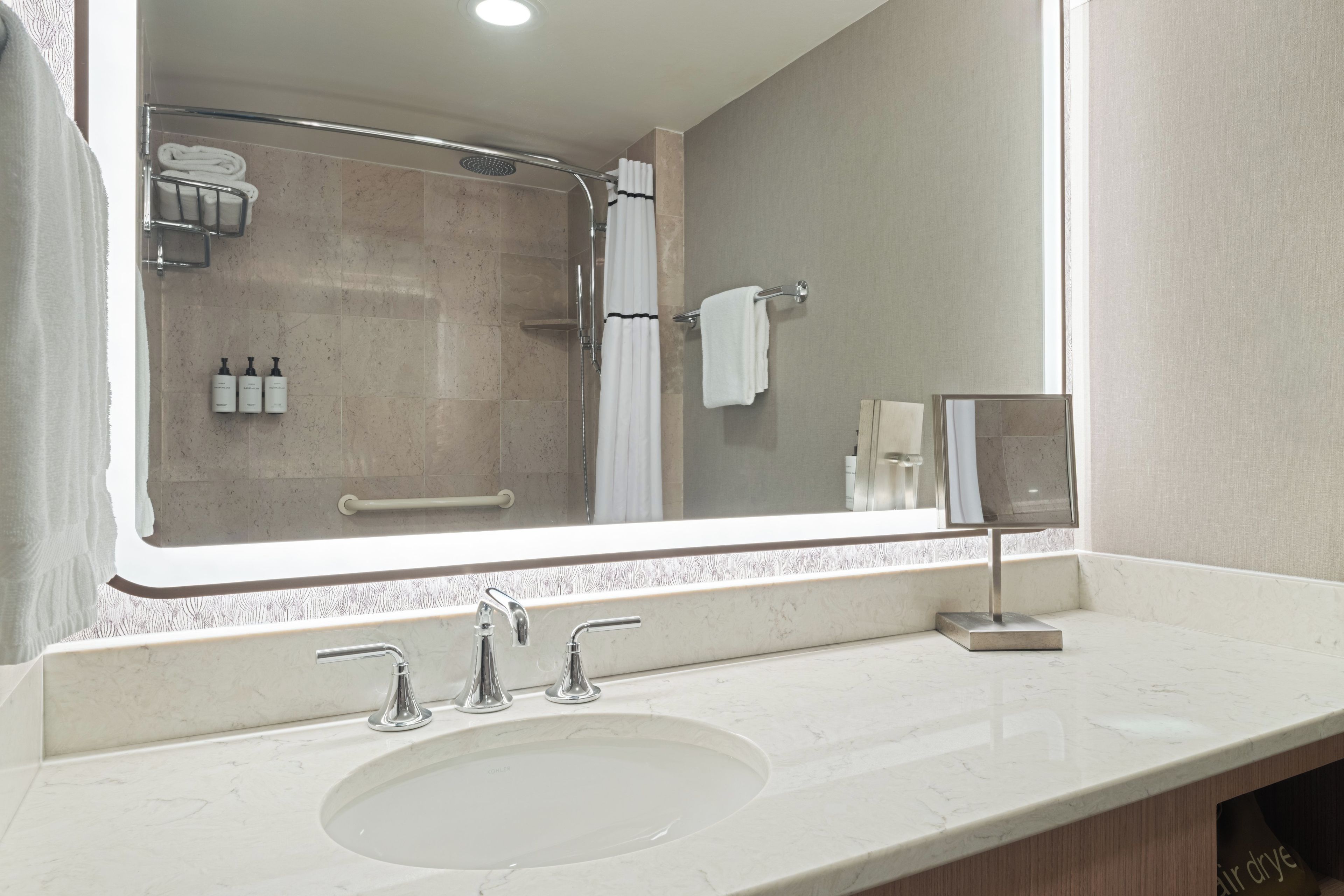 A bathroom with a large mirror, a sink with two faucets, and a shower area.