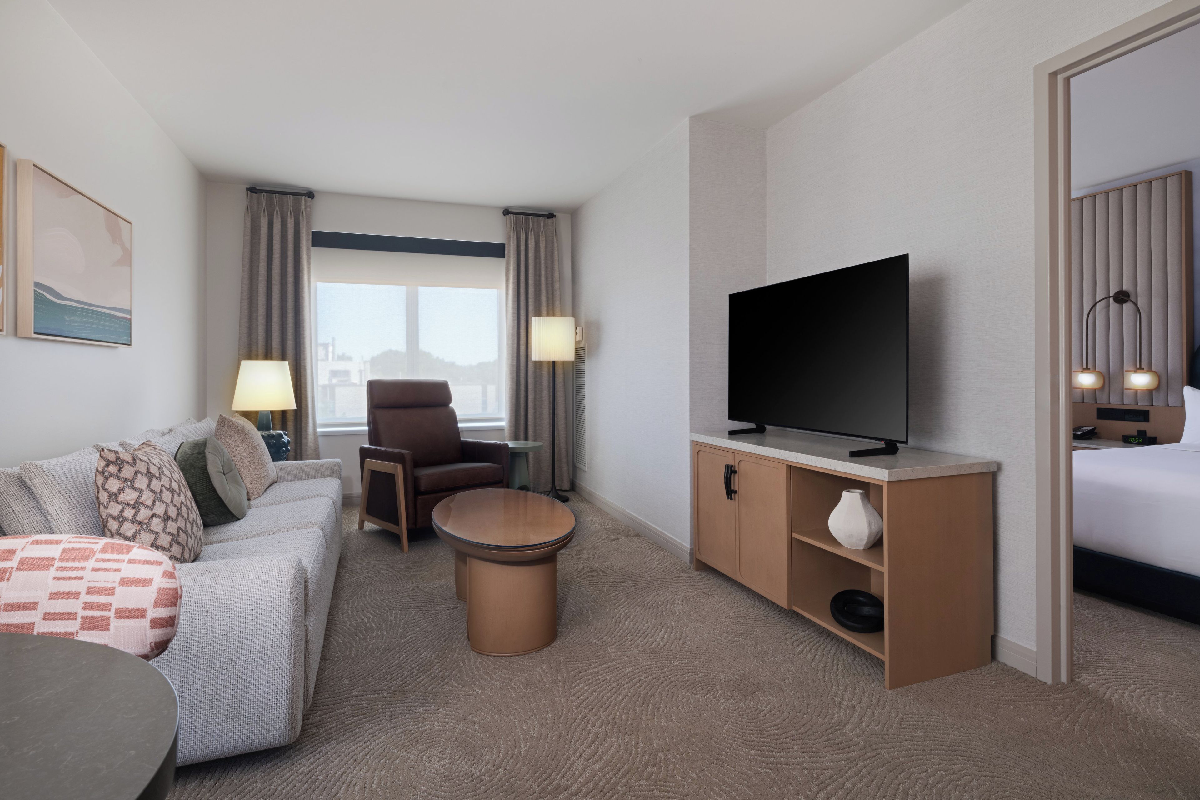 A hotel room with a sofa, armchair, TV, and a small table.