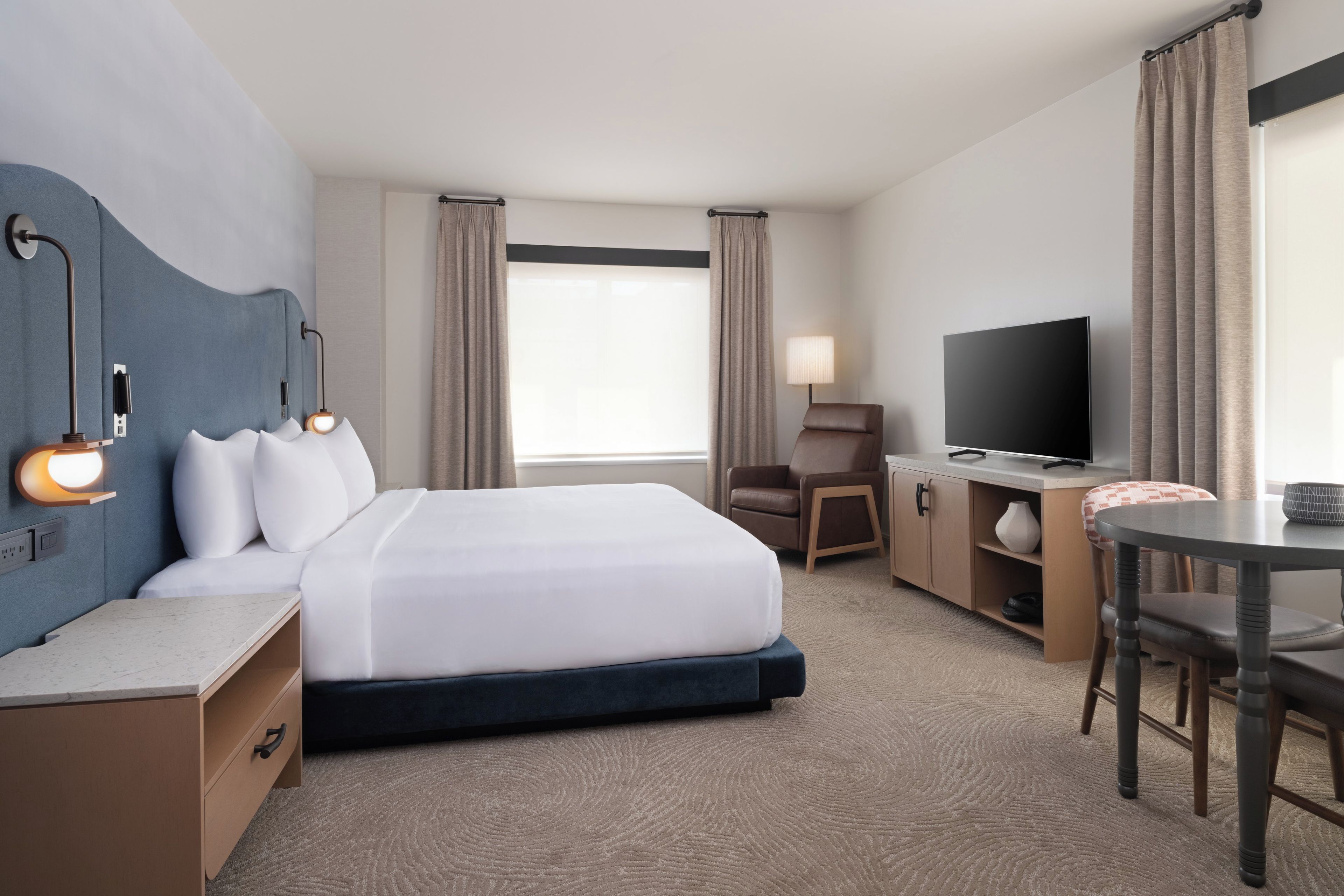 A hotel room with a bed, desk, chair, television, and a view of the outdoors.