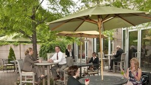 An outdoor patio area with round tables and chairs, some under umbrellas, and a few people seated. - InterContinental Suites Hotel Cleveland by IHG (Cleveland)