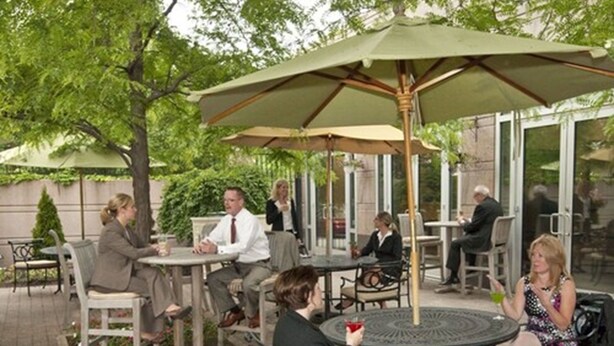 An outdoor patio area with round tables and chairs, some under umbrellas, and a few people seated. - InterContinental Suites Hotel Cleveland by IHG (Cleveland)