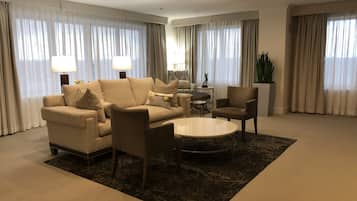 A spacious living room with a beige sofa, armchairs, a coffee table, and a side table with a lamp.