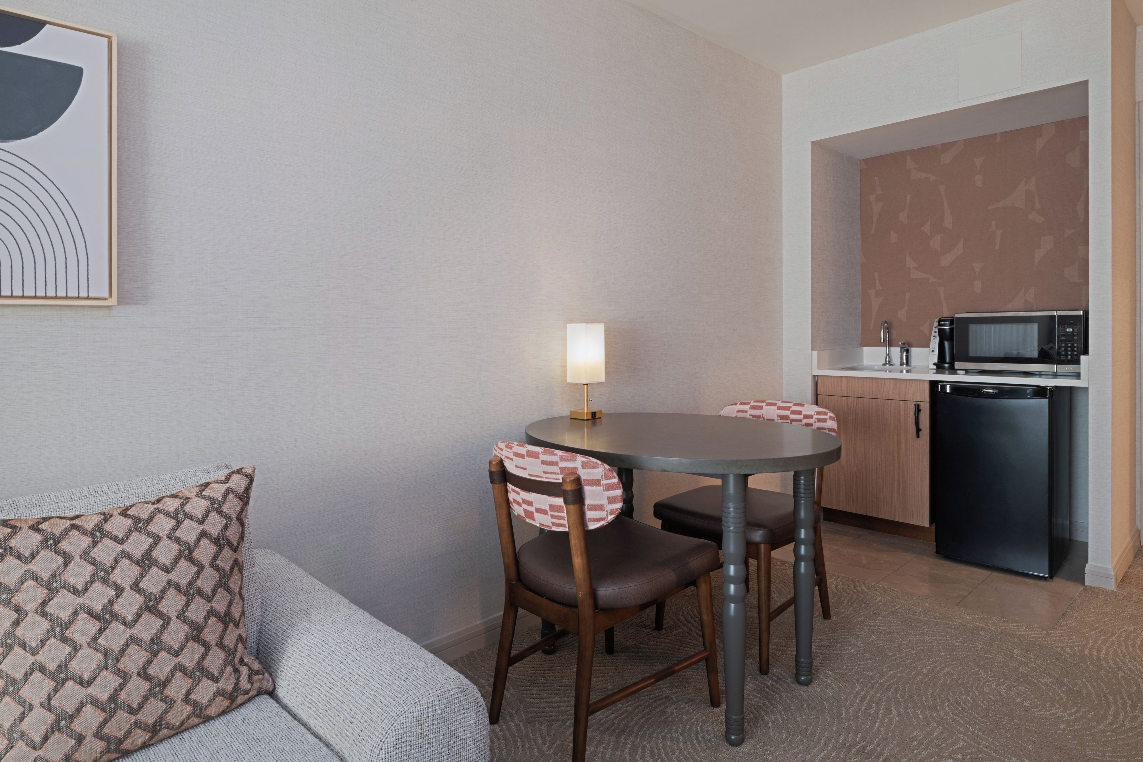 A compact hotel room with a dining table, two chairs, a sofa, a kitchen area with a microwave, and a refrigerator.