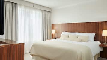 A hotel room with a large bed, wooden headboard, two bedside tables with lamps, and a desk with a chair.