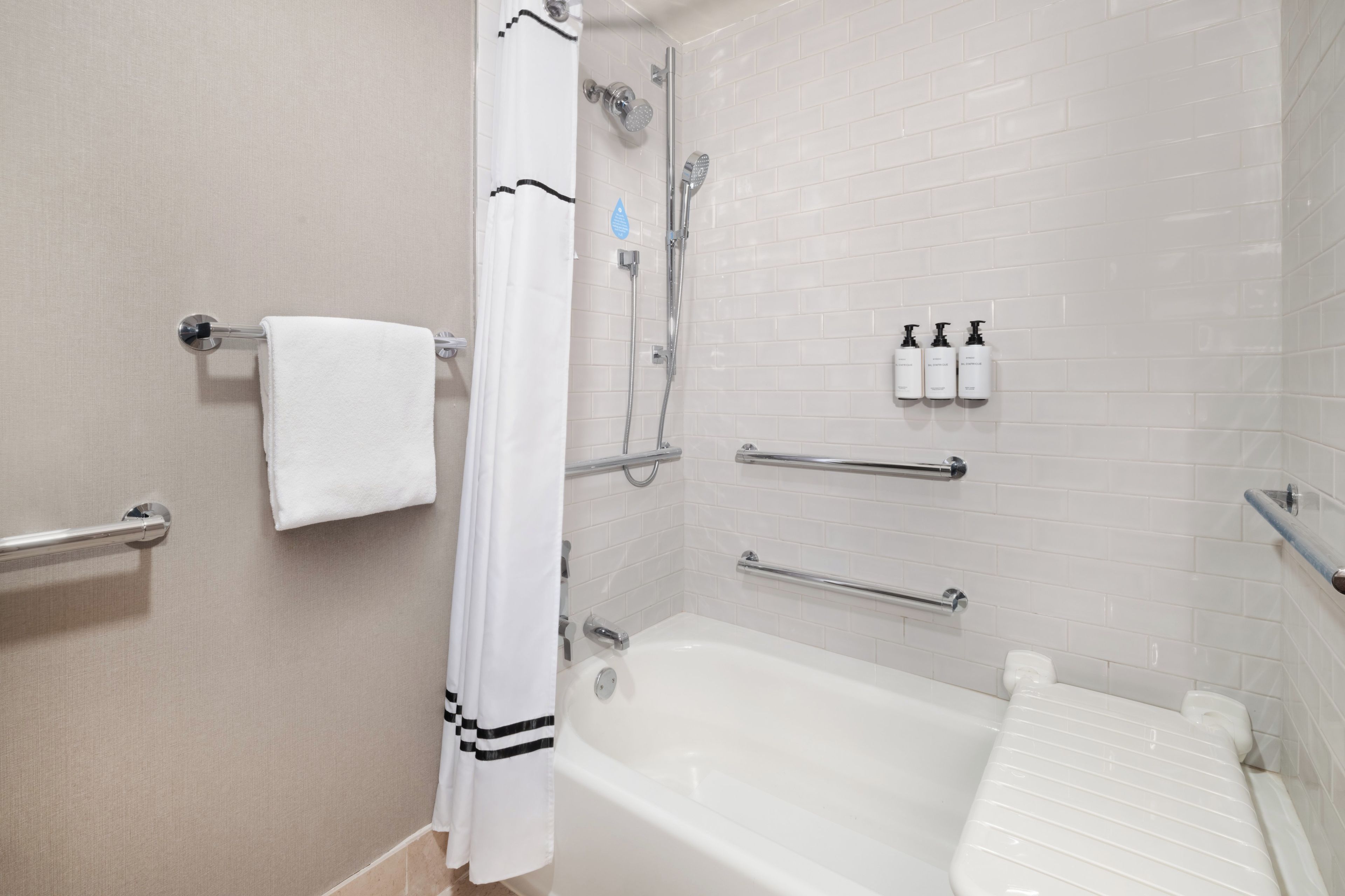 A bathroom with a bathtub, a shower, a towel rack, and a handrail.