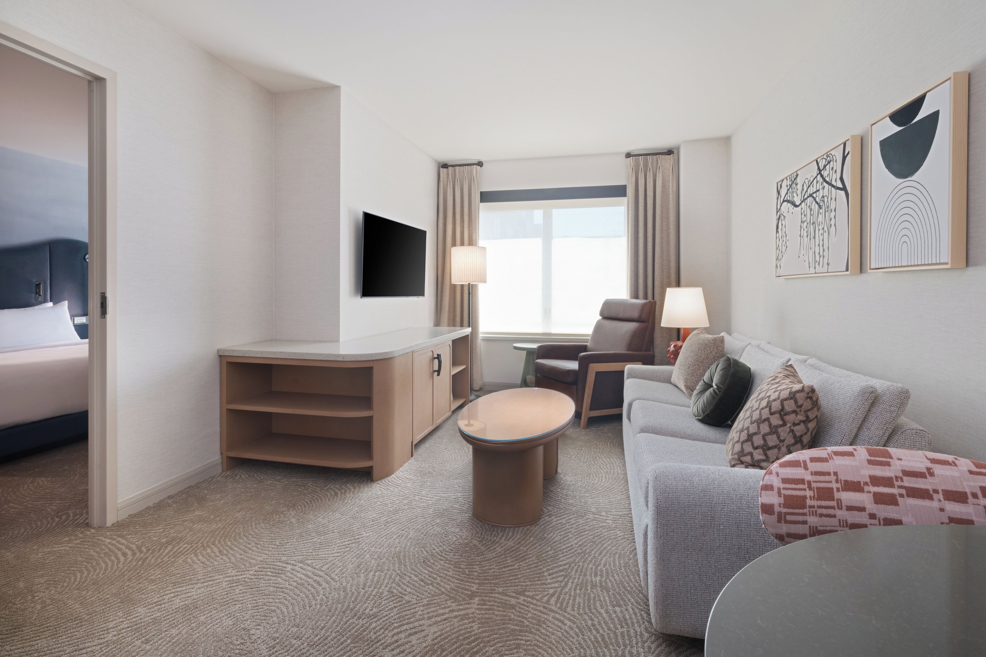 A hotel room with a bed, a TV, a desk, a chair, a sofa, and a small table.