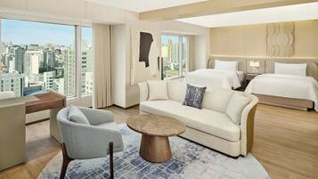 A modern hotel room with a city view, a sofa, a round coffee table, and a bed.