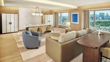 A modern hotel room with a dining area, a sofa set, a small table, and a view of the cityscape.