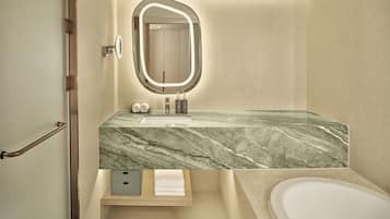 A modern bathroom with a marble sink, a large mirror with lighting, a bathtub, and a towel rack.