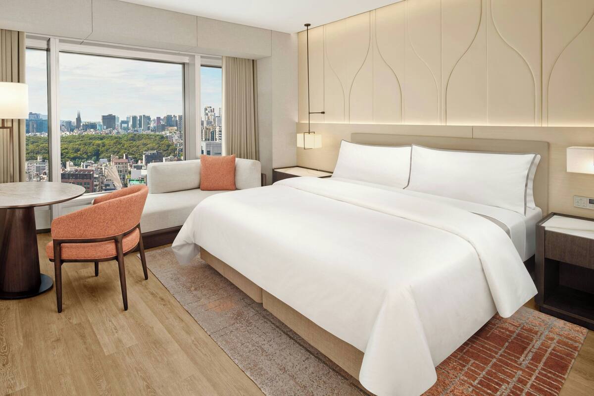 Une chambre d’hôtel dotée d’un grand lit, d’un coin salon avec une table et des chaises, et offrant une vue sur la ville.