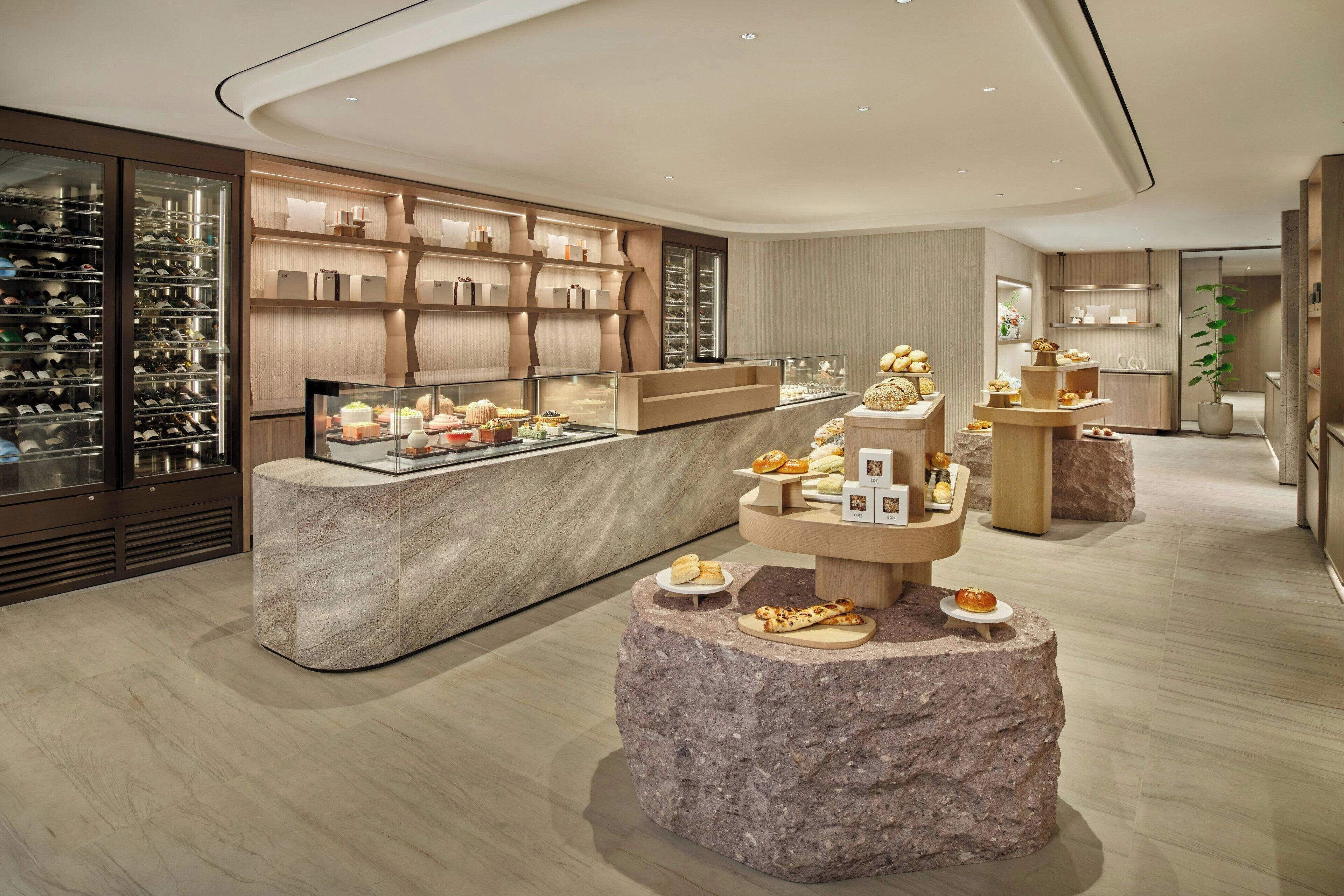 Un intérieur moderne avec un comptoir central où sont exposées des pâtisseries et, en arrière-plan, un meuble à vin.