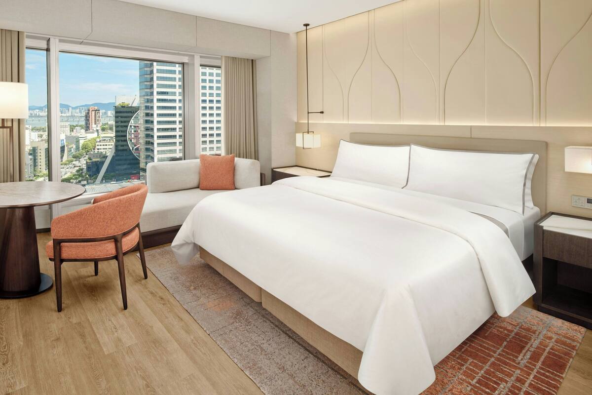 Une chambre d’hôtel avec un grand lit, un bureau, une chaise et une vue sur le paysage urbain.