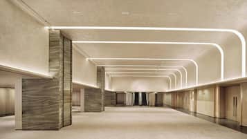 A spacious, modern hotel corridor with a minimalist design, featuring a marble column and a long, straight hallway with a uniform ceiling and lighting.