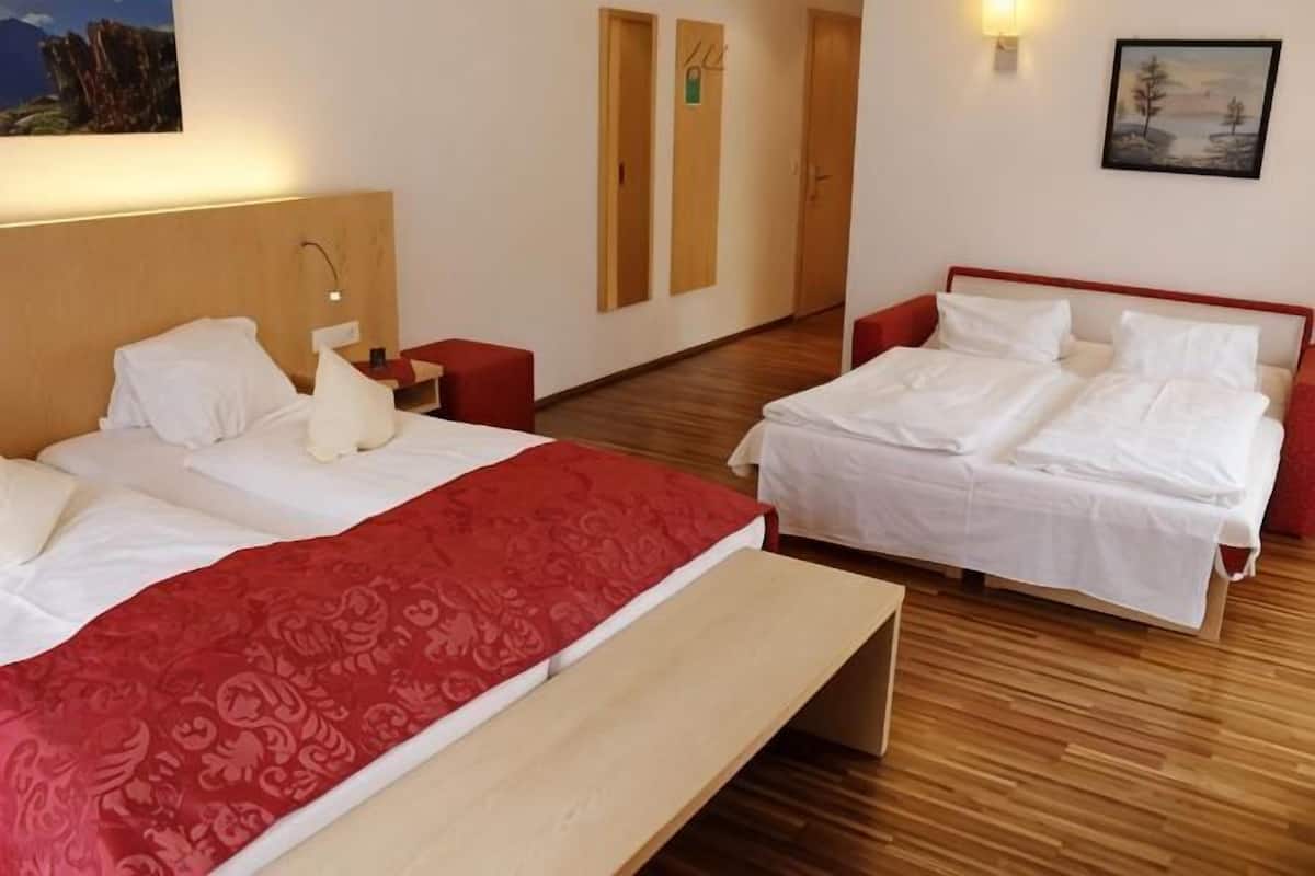 Een hotelkamer met twee bedden, een houten vloer, een bankje en een schilderij aan de muur.