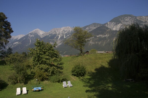 A grassy area with lounge chairs and a table, overlooking a mountain range. - Austria Classic Heiligkreuz (Hall In Tirol)