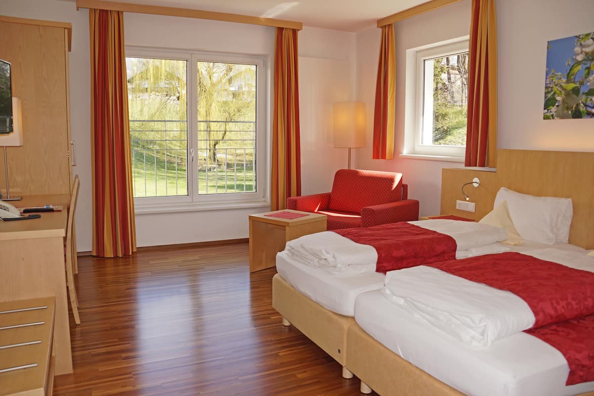 Een hotelkamer met twee bedden, een bureau, een stoel en een raam met gordijnen.