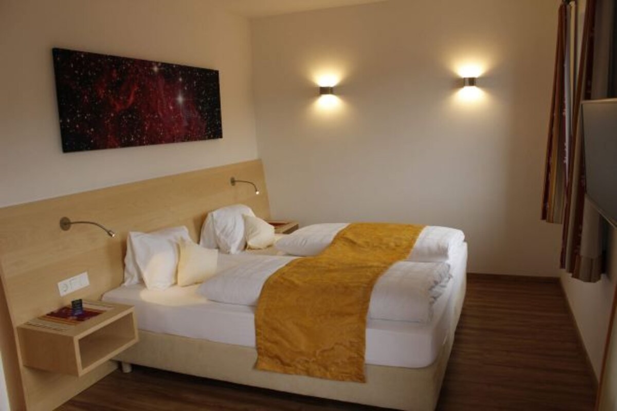 A hotel room with a bed, a nightstand, a wall-mounted painting, and two wall sconces.
